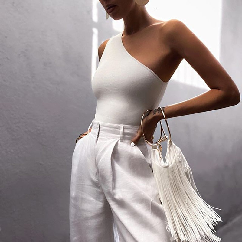 Frau in weißem One-Shoulder-Top und weißen Hosen mit Fransenhandtasche, elegant, modern.