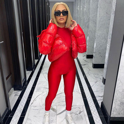 Frau in rotem Jumpsuit und roter Daunenjacke, blonde Haare, schwarze Sonnenbrille, weiße Turnschuhe.