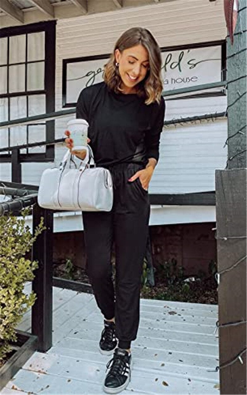 Frau in schwarzem Jumpsuit mit silberner Handtasche und Kaffee, lächelnd auf Veranda.