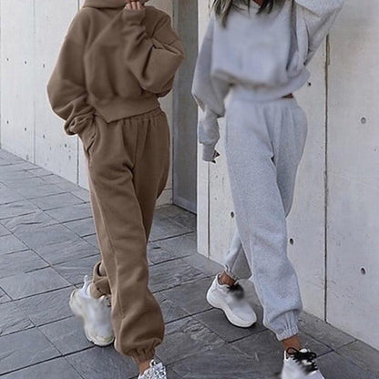 Zwei Frauen in bequemen Jogginganzügen, braun und grau, mit Kapuzenpullover und Jogginghose.