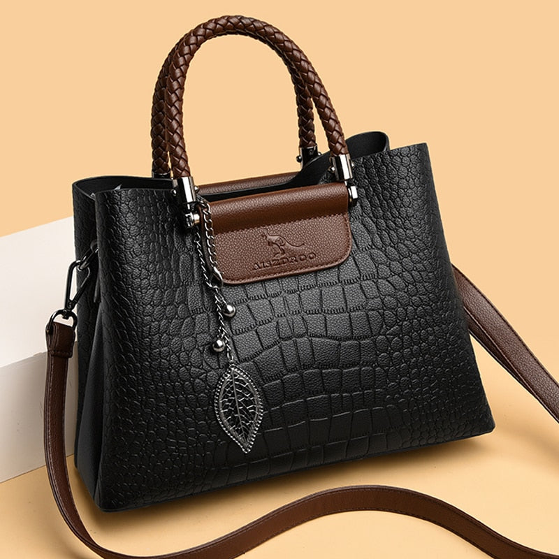 Schwarze Krokodilleder-Handtasche mit braunen Griffen und Blattanhänger, elegant und modisch.