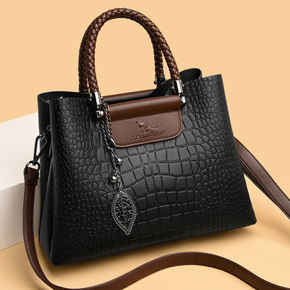 Schwarze Krokodilleder-Handtasche mit braunen Griffen und Blattanhänger, elegant und modisch.