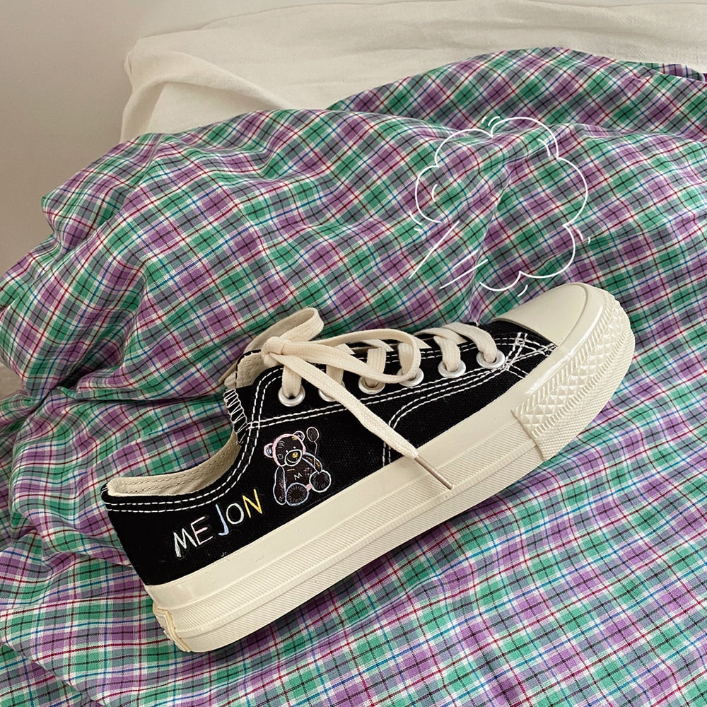 Schwarzer Sneaker mit Bärenstickerei, weißer Sohle und Schnürsenkeln auf kariertem Stoff.