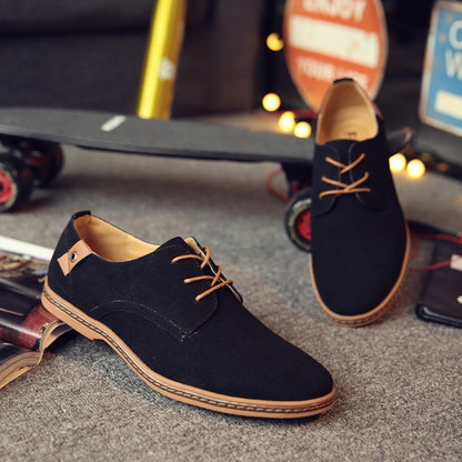 Schwarze Herren-Sneaker aus Wildleder mit braunen Schnürsenkeln auf grauem Teppich.