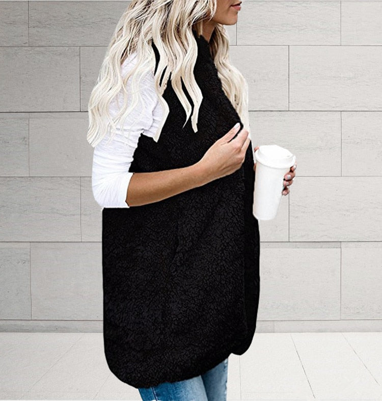 Frau in schwarzer Fleeceweste mit Kaffeebecher, weiße Bluse, blonde Haare, lässiger Stil.