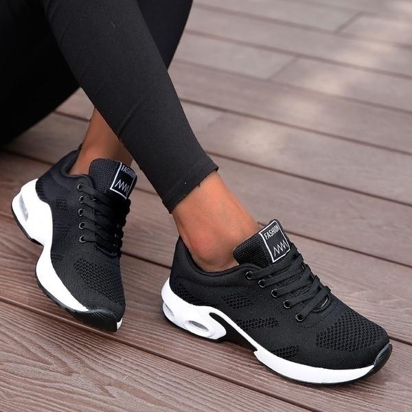 Schwarze Damen-Sneaker, atmungsaktiv, sportlich, mit weißer Sohle, auf Holzdeck.
