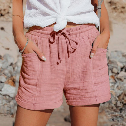 Frau trägt rosa Baumwollshorts mit Taschen, Sommermode, lässiger Stil, Strandhintergrund.