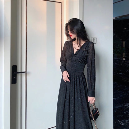 Frau in elegantem schwarzem Abendkleid mit langen Ärmeln, steht in modernem Innenraum.