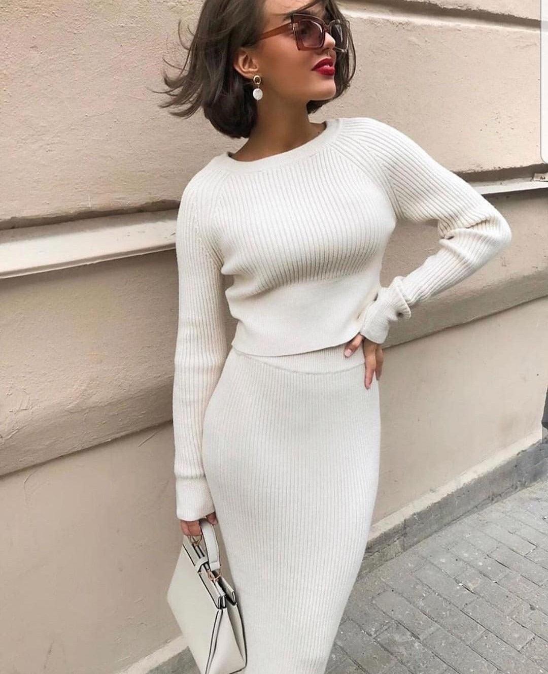Frau in weißem Strickkleid mit Handtasche, elegante Mode, Herbstoutfit, urbane Kulisse.