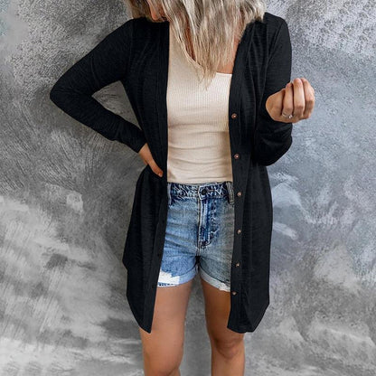 Frau in schwarzem Cardigan und Jeansshorts vor grauem Hintergrund.