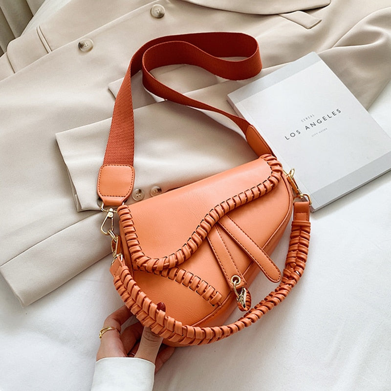 Orange Lederhandtasche mit geflochtenem Riemen auf beigem Mantel, modisch und elegant.