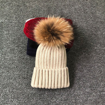 Beige Strickmütze mit Kunstfellbommel auf grauem Hintergrund, Wintermode Accessoire.
