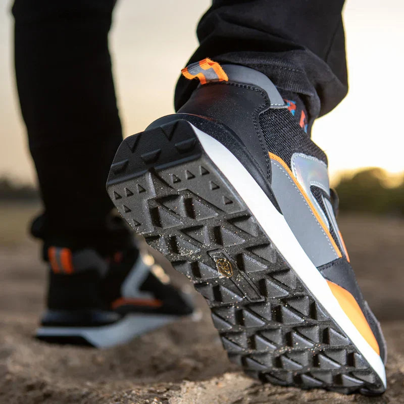 Schwarze und orangefarbene Laufschuhe mit rutschfester Sohle auf sandigem Untergrund.