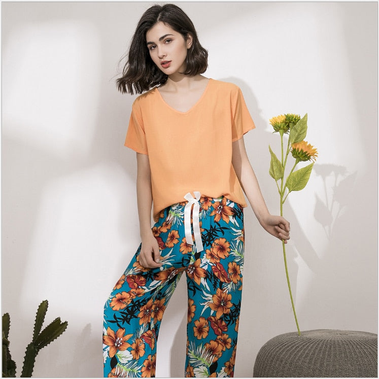 Frau in orangefarbenem T-Shirt und blumiger Hose mit Sonnenblume, modisch, sommerlich.