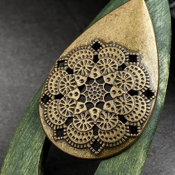 Bronzefarbener Mandala-Anhänger auf grünem Hintergrund, filigranes Design, Boho-Schmuck.