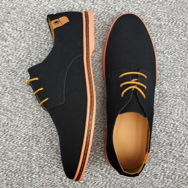 Schwarze Herrenschuhe aus Leder mit braunen Schnürsenkeln auf grauem Teppich.