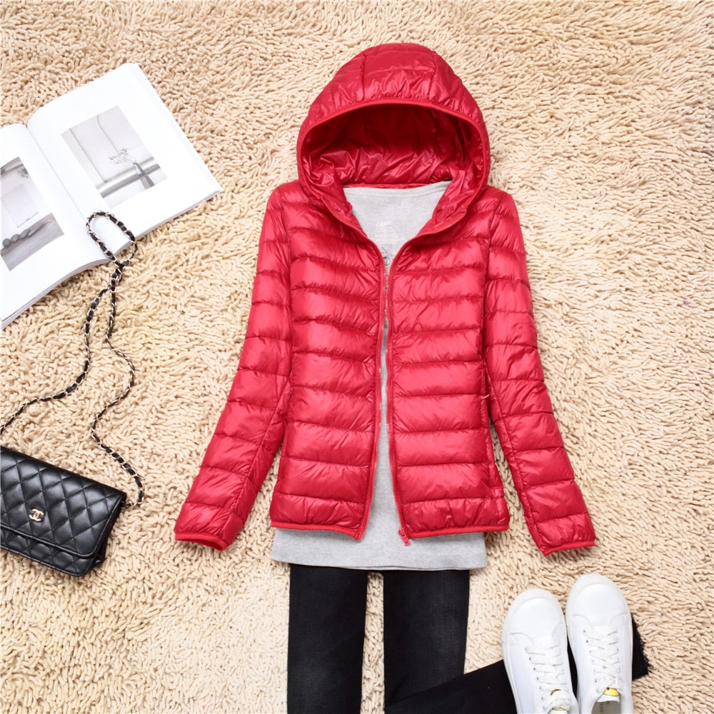 Rote Damen-Daunenjacke mit Kapuze, modisch, warm, auf Teppich mit Tasche und Schuhen.