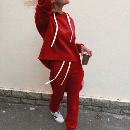 Frau in rotem Jogginganzug mit Kaffeebecher, weiße Sneakers, Freizeitmode, Straßenhintergrund.