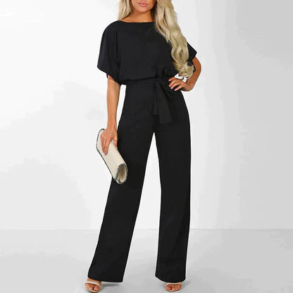 Frau in schwarzem Jumpsuit mit Gürtel, hält weiße Clutch, elegante Mode, Abendoutfit.