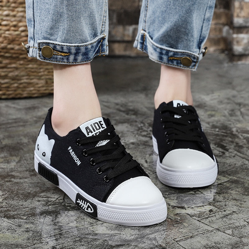 Schwarze Damen-Sneaker mit Katzenmotiv, weißer Sohle und Jeans-Details auf Betonboden.