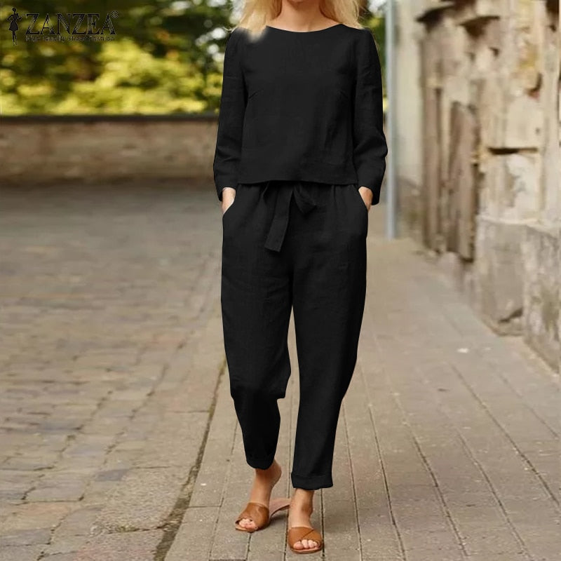 Frau in schwarzem Leinen-Jumpsuit, lässig, mit Taschen, auf Kopfsteinpflasterweg.