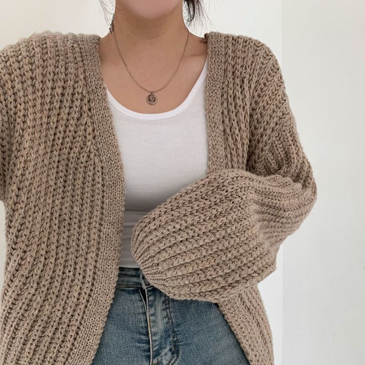 Frau trägt beige Strickjacke, weißes Top, blaue Jeans; modische Damenbekleidung, Herbstmode.