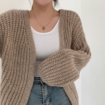 Frau trägt beige Strickjacke, weißes Top, blaue Jeans; modische Damenbekleidung, Herbstmode.
