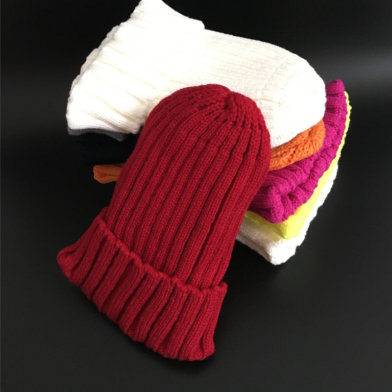 Rote Strickmütze aus Wolle, gestapelt auf bunte Wollsocken, Wintermode Accessoires.