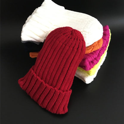 Rote Strickmütze aus Wolle, gestapelt auf bunte Wollsocken, Wintermode Accessoires.