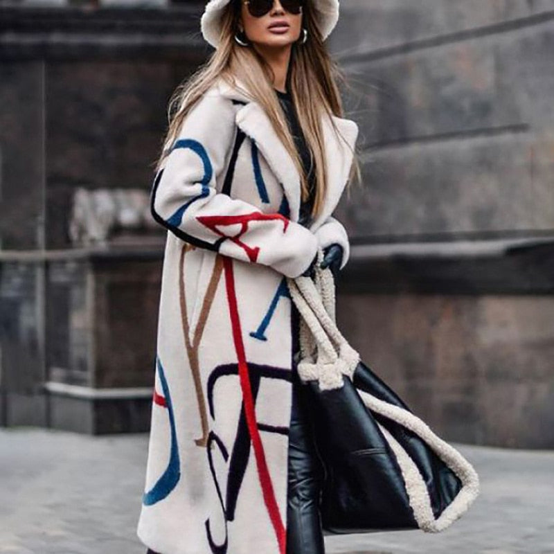 Frau in weißem Mantel mit buntem Muster, schwarzer Tasche, Sonnenbrille und Hut auf Stadtstraße.
