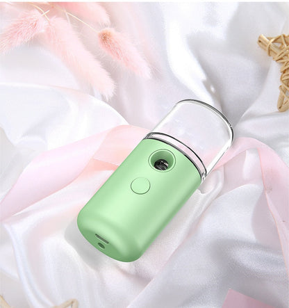 Grüner tragbarer Gesichtsdampfer auf weißem Seidentuch, Hautpflegegerät, USB-aufladbar.