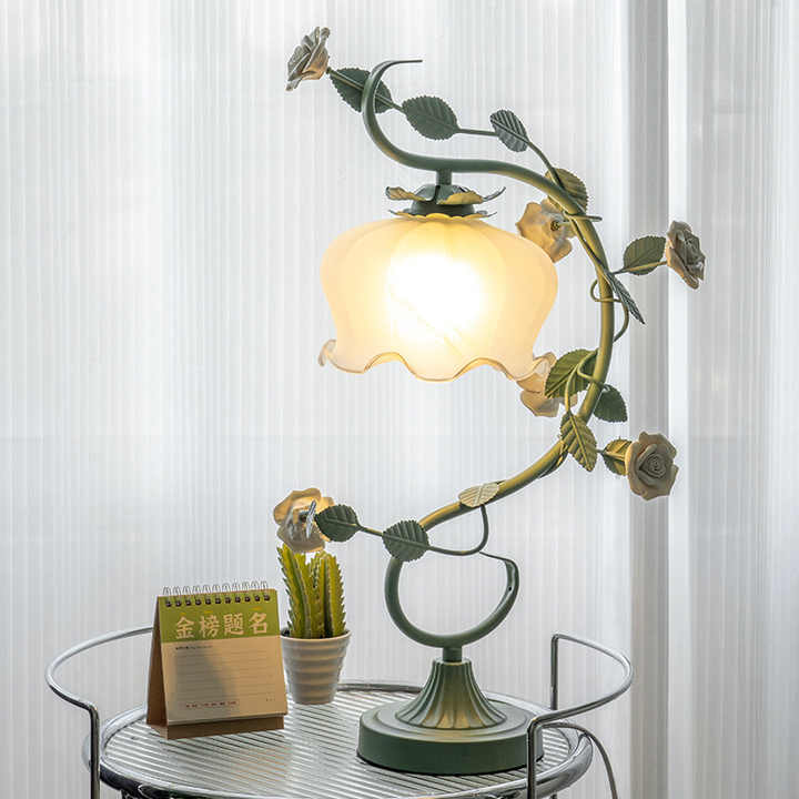 Grüne Tischlampe mit Blumenmotiv, Vintage-Stil, auf rundem Tisch vor hellem Vorhang.