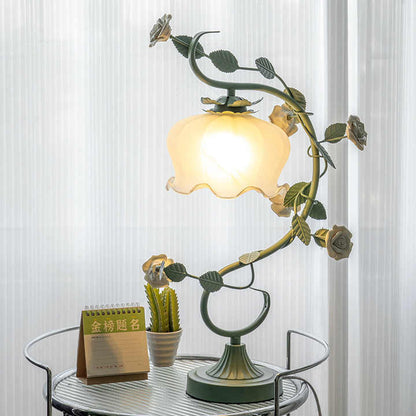 Grüne Tischlampe mit Blumenmotiv, Vintage-Stil, auf rundem Tisch vor hellem Vorhang.