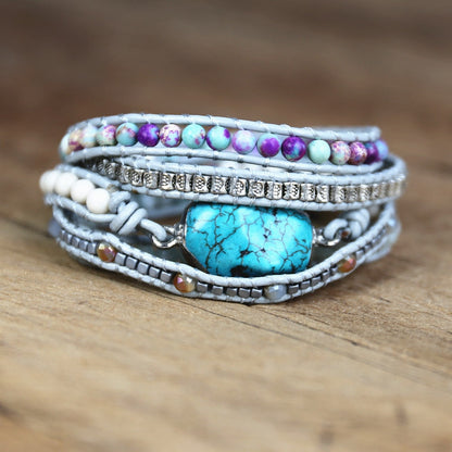 Mehrlagiges Armband mit türkisfarbenem Stein, Perlen und Strass auf Holzoberfläche.