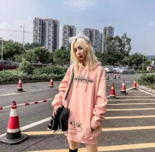 Frau in rosa Kapuzenpullover mit Cartoon-Design, Stadtlandschaft im Hintergrund.