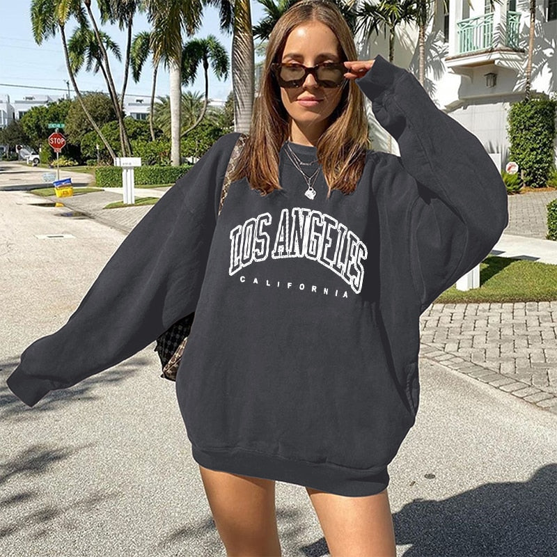 Frau in schwarzem "Los Angeles" Oversize-Pullover, Sonnenbrille, Straße, Palmen, lässige Mode.