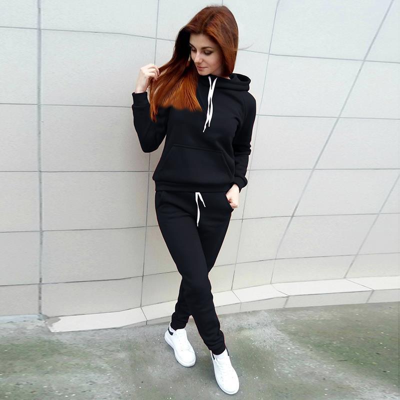 Frau in schwarzem Hoodie und Jogginghose, weiße Sneaker, lässige Sportbekleidung, urbaner Stil.
