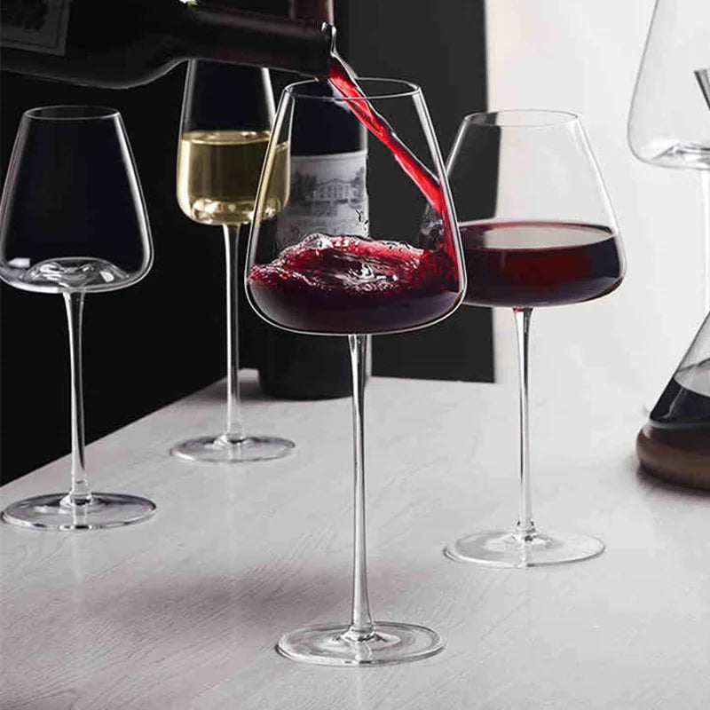 Rödvin hälls från en flaska i ett glas bland flera glas på ett bord 2