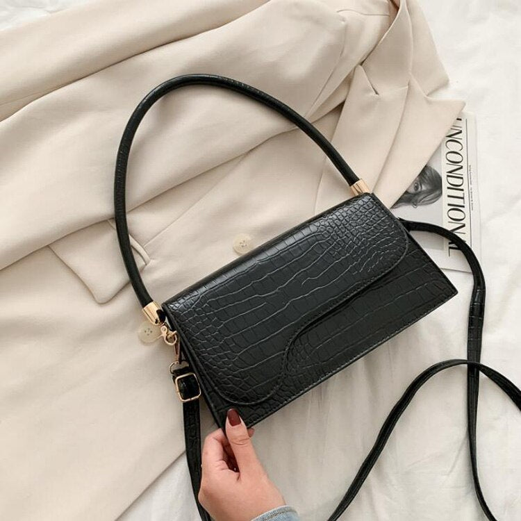 Schwarze Krokodilleder-Handtasche, elegant, Damenmode, Schulterriemen, auf beigem Mantel.