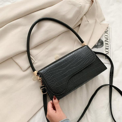 Schwarze Krokodilleder-Handtasche, elegant, Damenmode, Schulterriemen, auf beigem Mantel.
