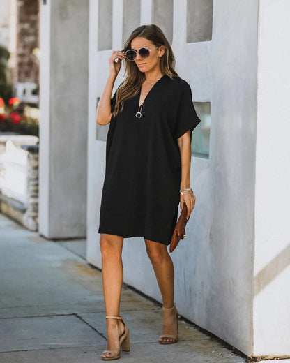 Frau in schwarzem Sommerkleid, Sonnenbrille, Sandalen, braune Clutch, modisch, urbaner Stil.