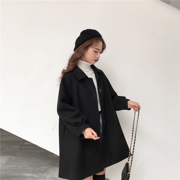 Frau in schwarzem Wollmantel und Baskenmütze, hält eine Kettentasche, modisch, elegant.