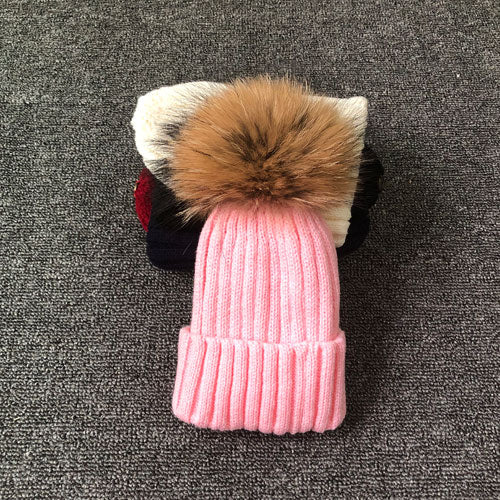 Rosa Strickmütze mit Kunstpelzbommel auf grauem Hintergrund, Wintermode Accessoire.