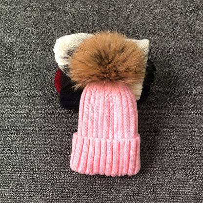 Rosa Strickmütze mit Kunstpelzbommel auf grauem Hintergrund, Wintermode Accessoire.