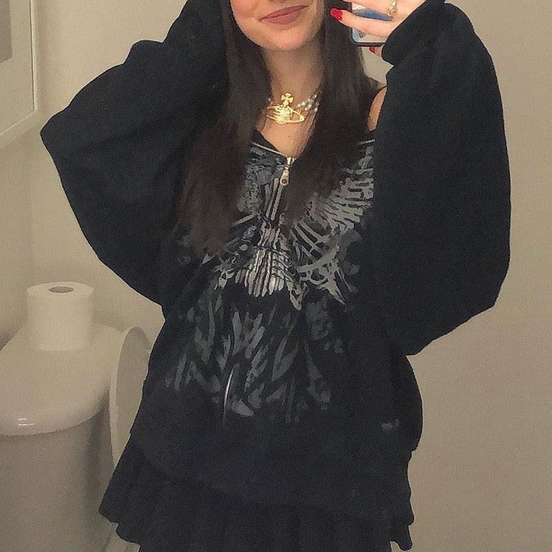 Frau in schwarzem Kapuzenpullover mit Totenkopf-Design, schwarzer Rock, modisches Outfit.