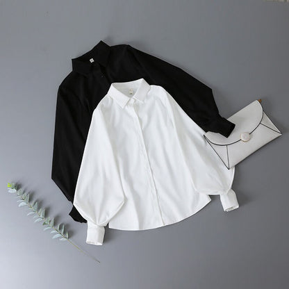 Schwarze und weiße Bluse aus Baumwolle mit Umschlagtasche auf grauem Hintergrund.