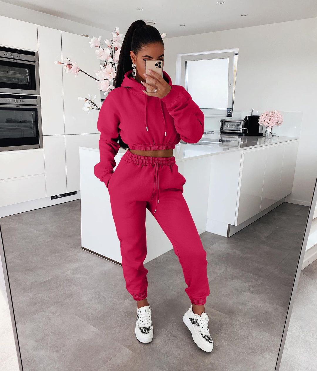 Frau in rotem Jogginganzug, Kapuzenpullover, Sneakers, moderne Küche, Spiegel-Selfie.