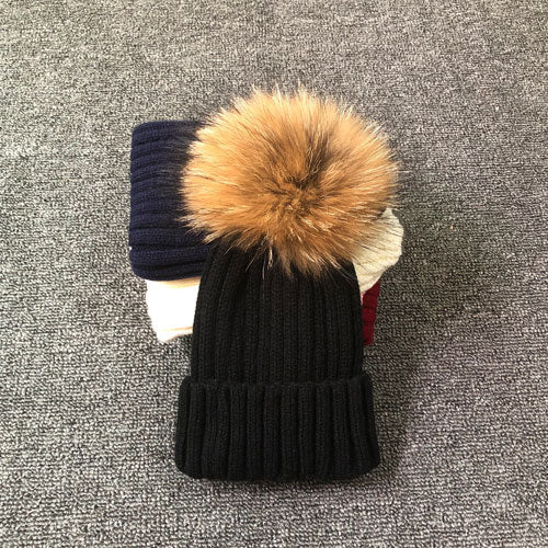 Schwarze Strickmütze mit Kunstfellbommel auf grauem Hintergrund, Wintermode Accessoire.