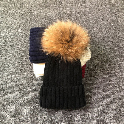 Schwarze Strickmütze mit Kunstfellbommel auf grauem Hintergrund, Wintermode Accessoire.