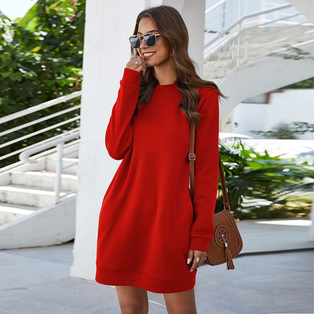 Frau im roten Sweatshirt-Kleid, braune Tasche, Sonnenbrille, lächelnd, draußen.